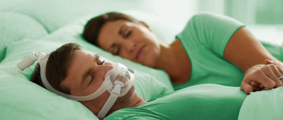 Man in groen t-shirt slaapt met een masker en vrouw in groen t-shirt slaapt naast hem