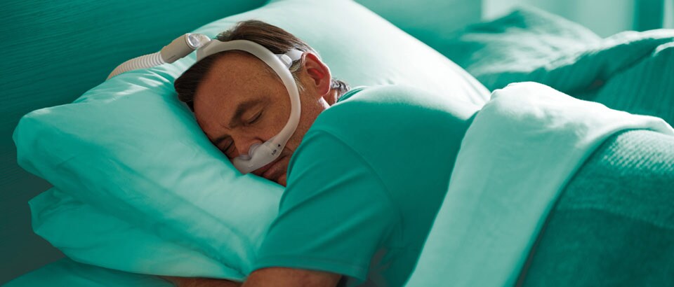 Man in een groen t-shirt met een masker, slaapt op zijn buik