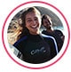 Profielfoto van reviewer, een jonge vrouw in wetsuit lachend op een strand.