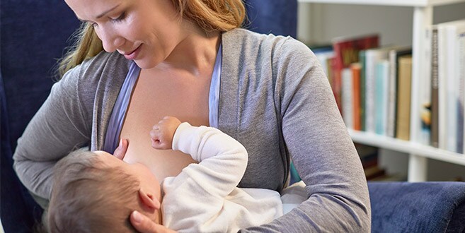 Een moeder laat de doorgeschoven houding zien terwijl ze borstvoeding geeft en de baby ondersteunt met één arm en haar borst met de andere.