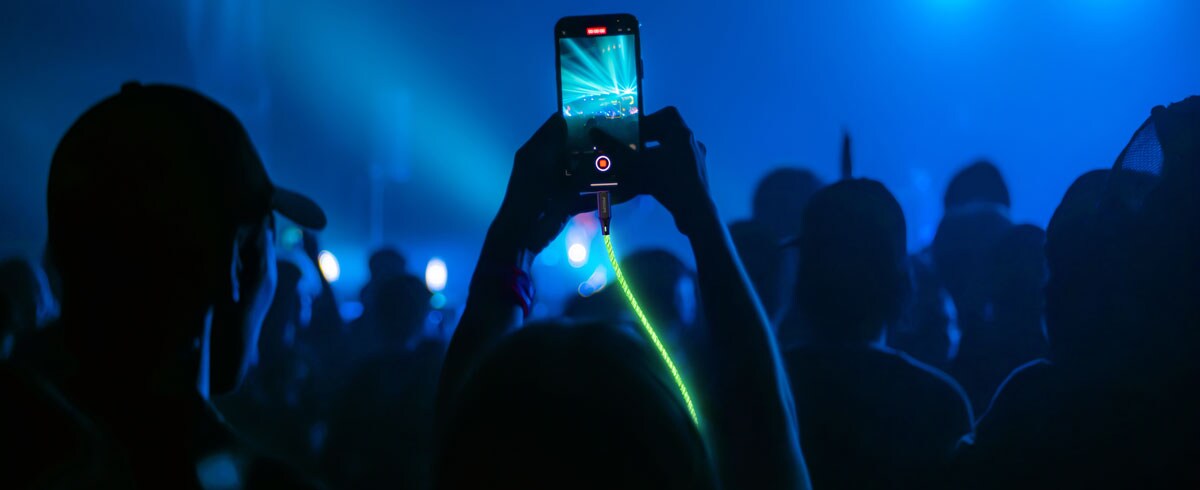 Een persoon tilt voor een groot publiek een mobiele telefoon op die verbonden is aan een stralende kabel om een evenement vast te leggen