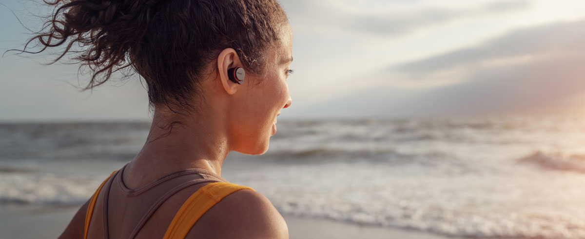 Vrouw met een volledig draadloze Philips-sportkoptelefoon op het strand