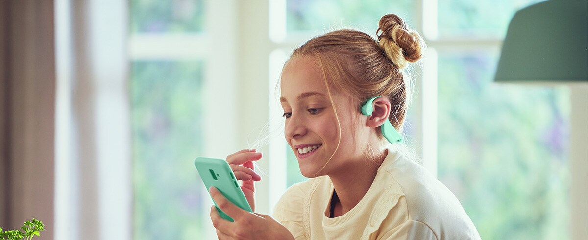 Een meisje dat groene bone conduction kinderkoptelefoons gebruikt.