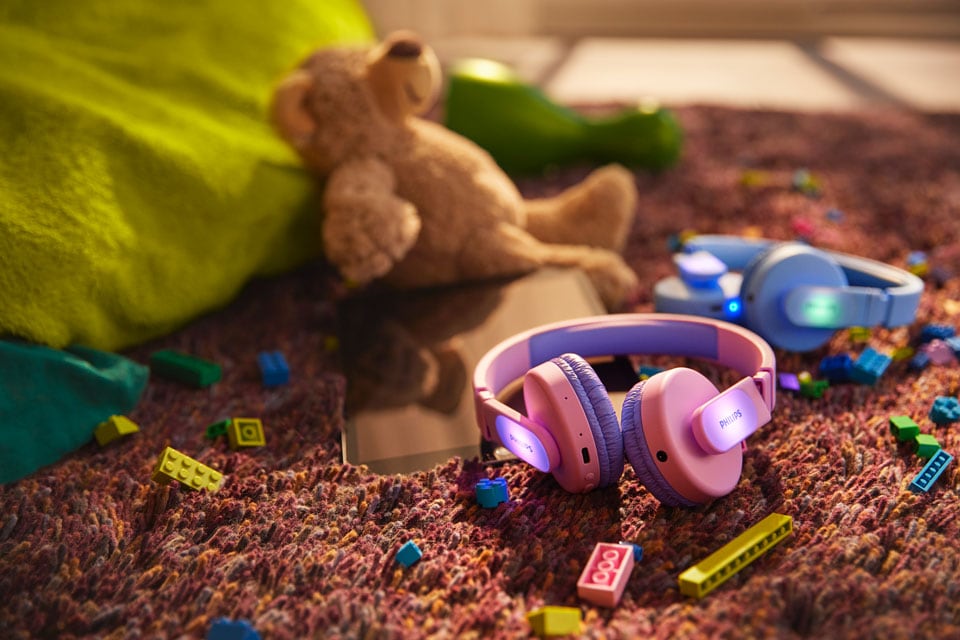 Een blauwe en een roze kinderkoptelefoon op de grond met speelgoed.