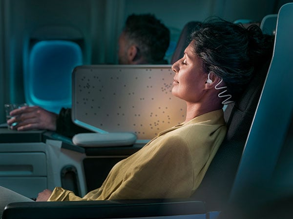 Vrouw die slaapt in het vliegtuig terwijl ze de Philips TAN7808 slaap-oordopjes gebruikt