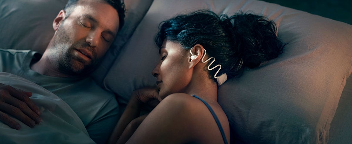 Vrouw die naast haar man slaapt terwijl ze Philips N7808 slaap-oordopjes met Kokoon draagt