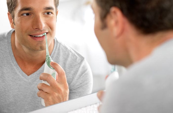 Een man kijkt naar zijn spiegelbeeld terwijl hij zijn witte tanden poetst met een elektrische tandenborstel.