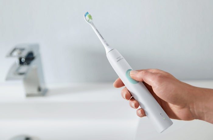 Iemand houdt een witte Philips Sonicare elektrische tandenborstel vast.