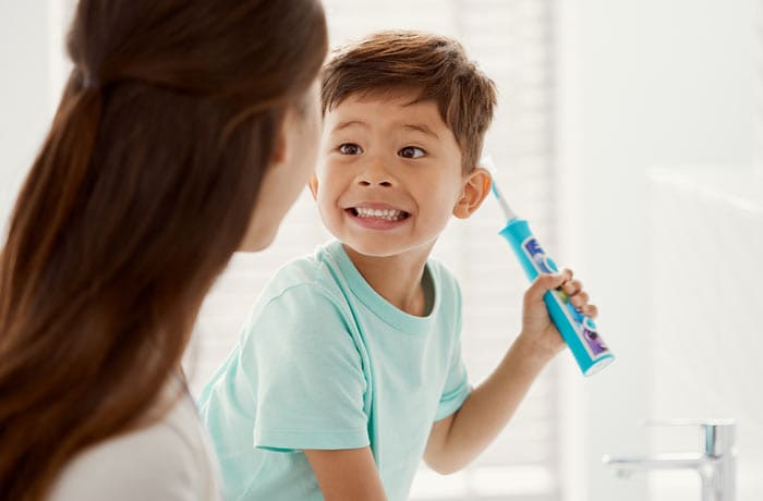 Een jongetje grijnst naar zijn moeder terwijl hij een blauwe Philips Sonicare for Kids-tandenborstel vasthoudt.