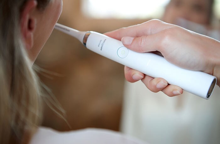 Een close-up van een vrouw die haar tanden poetst met een witte Philips Sonicare elektrische tandenborstel.