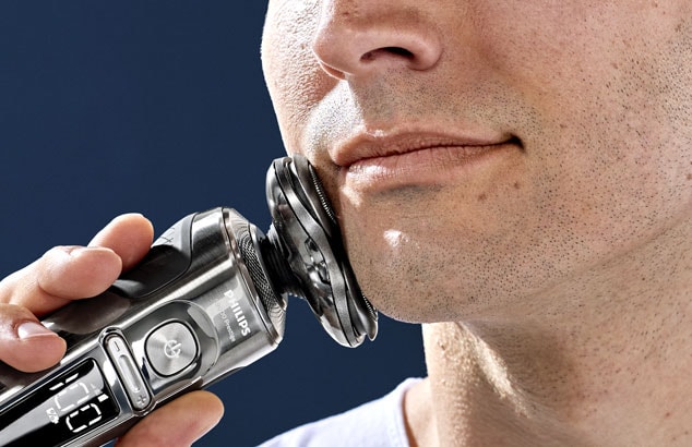 Close-up van de kin van een man met korte stoppels die een Philips OneBlade tegen zijn kaak drukt.