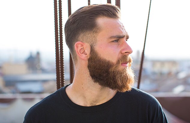 Zijprofiel van man met een lange, bruine baard en kort, bruin haar met een stad op de achtergrond.