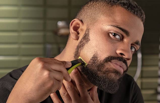 Een man scheert zijn korte baard verticaal van zijn wang tot aan zijn kaaklijn, met als resultaat een gladgeschoren plek.  