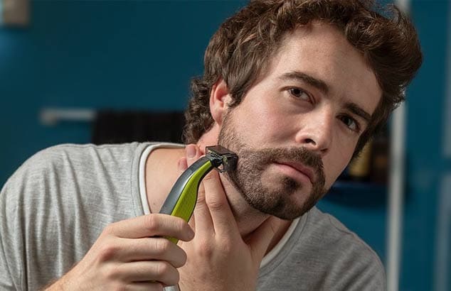 Een jongeman gebruikt een trimmer met een speciaal hulpstuk om een warrige baard te trimmen.
