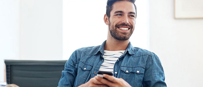 Een man met een overhemd met stoppelbaard houdt een telefoon vast terwijl hij glimlacht.