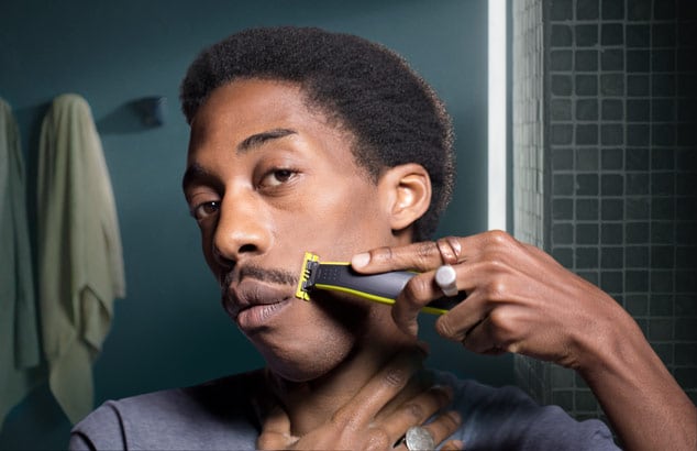 Een jongeman met donkerke huidskleur trimt zijn snor met de Philips OneBlade voor een spiegel in een badkamer