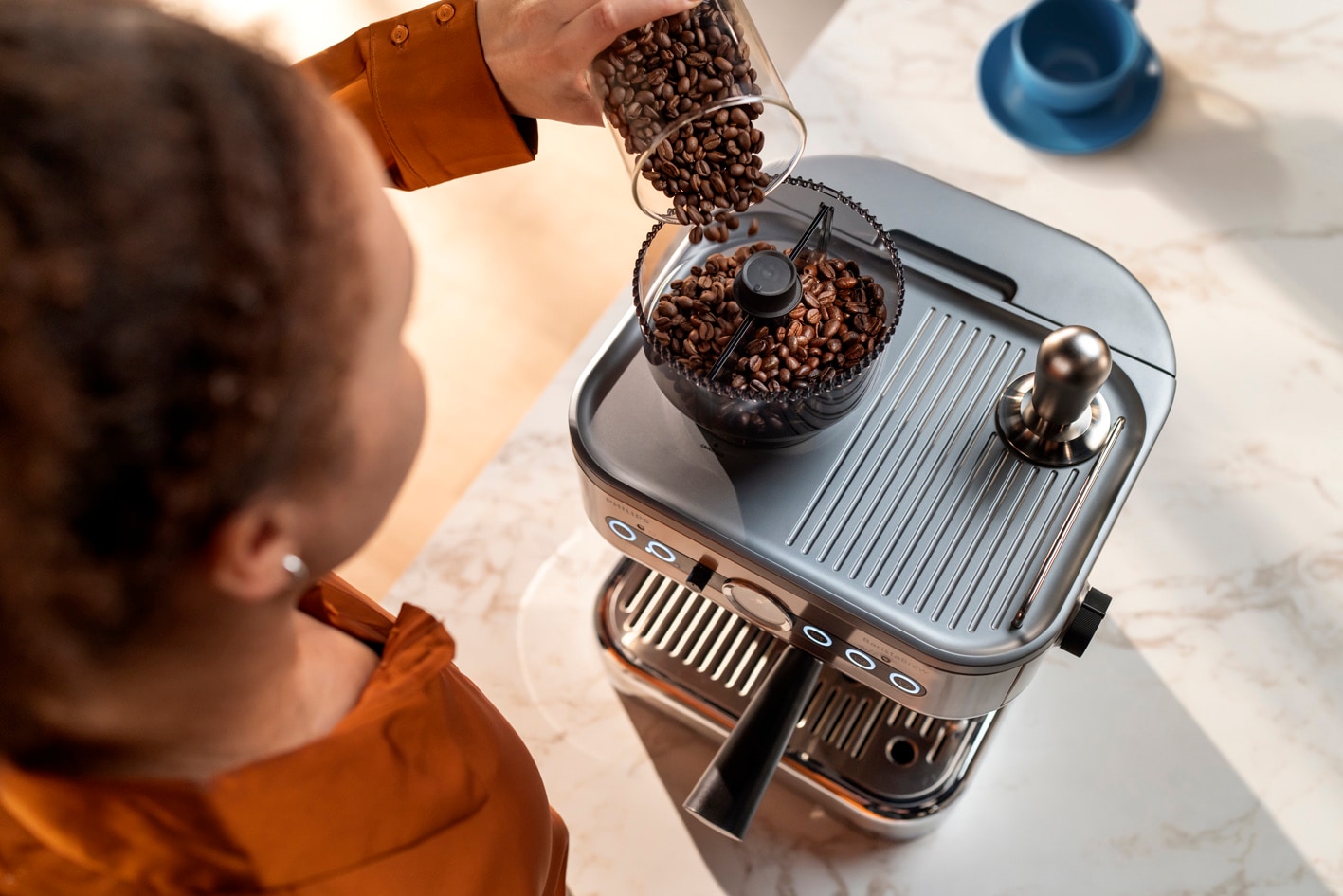 Een jonge vrouw giet koffiebonen in de koffiebonenbak van de Philips Barista