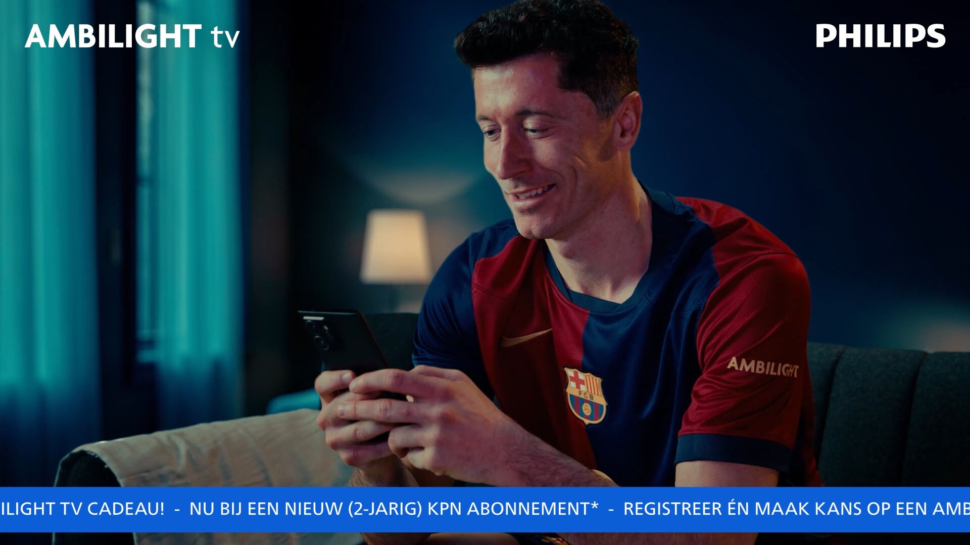 Robert Lewandowski zit op de bank in een FC Barcelona-shirt en kijkt glimlachend op zijn telefoon, met Ambilight- en Philips-logo’s zichtbaar op het scherm.