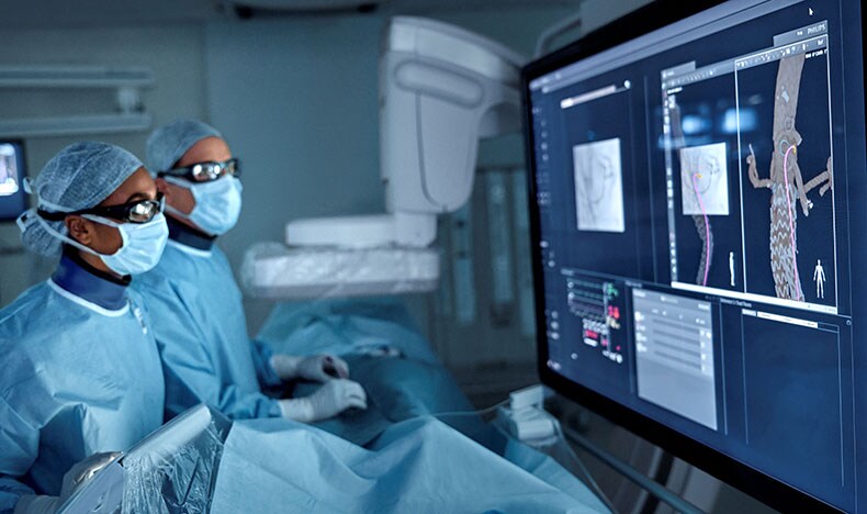 An extreme close-up of a surgeon’s face shows them wearing a mask and protective eyewear, the latter reflecting an image from a patient monitor